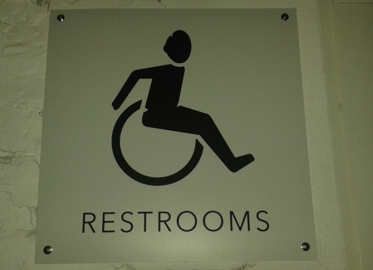 Foto: Schild mit Grafik von einem Rollstuhlfahrer, dessen Arme in Bewegung nach hinten gerichtet sind, um den Rollstuhl zu bewegen