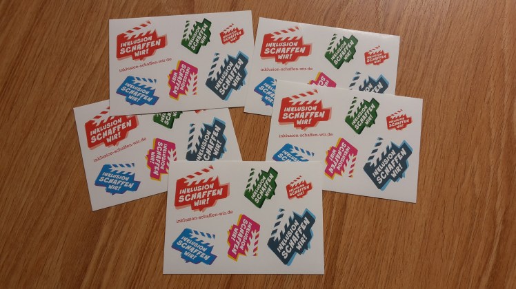Foto: 5 Postkarten mit bunten Logo-Aufklebern von "Inklusion schaffen wir"