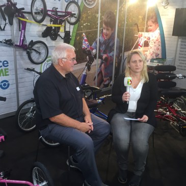 Foto: Nadine sitzt auf der REHACARE 2017 mit einem Mikrofon in der Hand neben ihrem Interviewpartner Bob